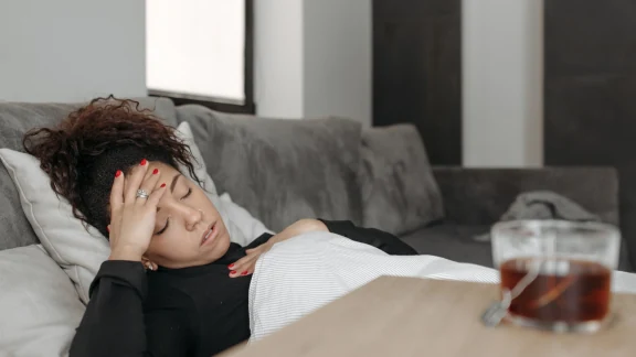 Woman resting on a couch with a cup of tea, exhausted